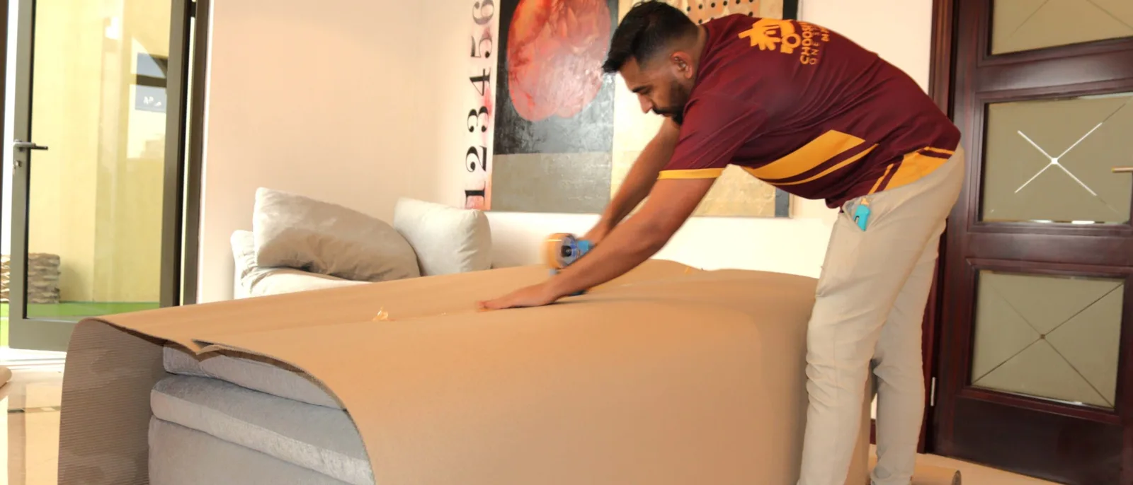 A mover wrapping a sofa in brown paper in a living room